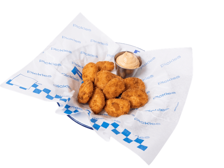 Nuggets de frango empanados servidos sobre papel com pote de maionese ao lado