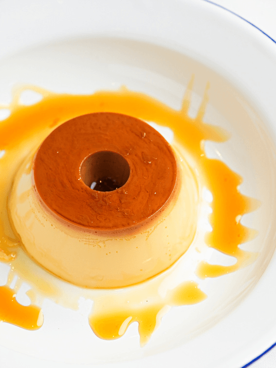 Pudim de leite condensado com calda de caramelo escorrendo, em prato branco