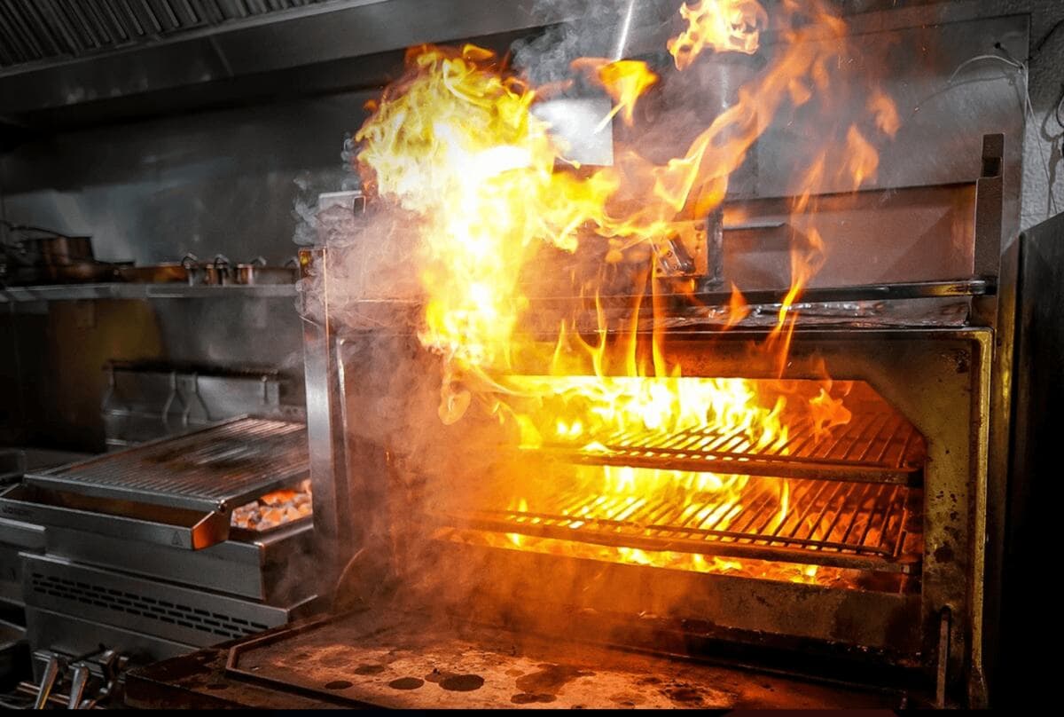 Interior de um forno Josper aceso: labareda alta subindo entre as duas grelhas, na cozinha